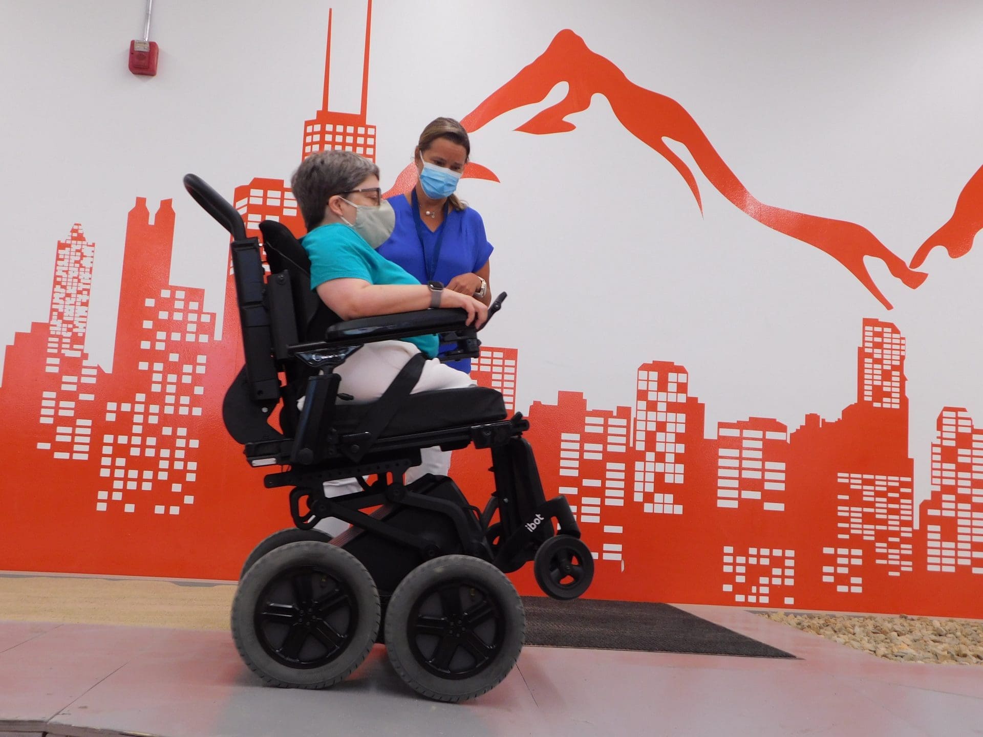iBOT user in 4-Wheel Mode driving through the obstacle course at Mobius Mobility, alongside a Mobius Mobility clinician